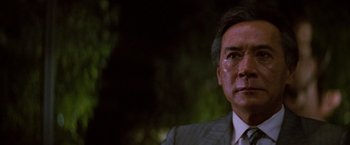 Movie still from “Die Hard” (1988), directed by John McTiernan – An older man wearing a suit and tie looking at the camera; Close Up shot, Low angle