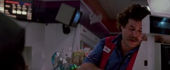 Movie still from “Die Hard” (1988), directed by John McTiernan – A man wearing a red and blue shirt is in front of a television; Close Up shot, Low angle