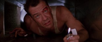 Movie still from “Die Hard” (1988), directed by John McTiernan – A person laying on the ground holding a lighter; Close Up shot, Low angle