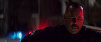 Movie still from “Die Hard” (1988), directed by John McTiernan – A man in a police uniform sitting in front of a building; Close Up shot, Low angle