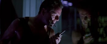 Movie still from “Die Hard” (1988), directed by John McTiernan – A man smoking a cigarette while looking at a cell phone; Close Up shot, Low angle
