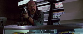 Movie still from “Die Hard” (1988), directed by John McTiernan – A man with long hair is looking at a cell phone; Medium shot, Low angle