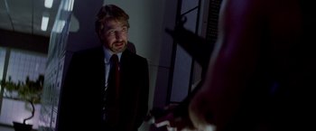 Movie still from “Die Hard” (1988), directed by John McTiernan – A man wearing a suit and tie in a dark room; Medium shot, Over the shoulder angle