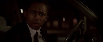 Movie still from “Die Hard” (1988), directed by John McTiernan – A man wearing a suit and tie sitting in a car; Close Up shot, Low angle