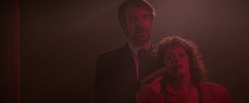 Movie still from “Die Hard” (1988), directed by John McTiernan – A man holding a gun and a woman in a dark room; Close Up shot, Low angle