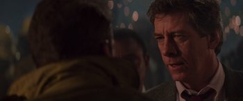 Movie still from “Die Hard” (1988), directed by John McTiernan – Two men are standing in a room with lights in the background; Close Up shot, Over the shoulder angle