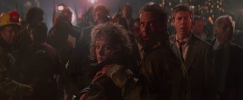 Movie still from “Die Hard” (1988), directed by John McTiernan – A man and a woman are standing in front of a group of people; Medium shot, Low angle