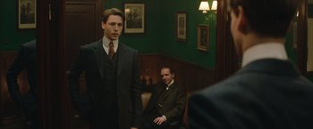 Movie still from “The King's Man” (2021), directed by Matthew Vaughn – A man in a suit and tie standing next to another man in a suit and tie; Medium shot, Over the shoulder angle