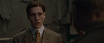 Movie still from “The King's Man” (2021), directed by Matthew Vaughn – A man in a suit and tie standing in front of a wall; Close Up shot, Low angle