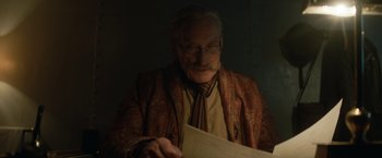 Movie still from “The King's Man” (2021), directed by Matthew Vaughn – An old man wearing a suit and tie reading a piece of paper; Close Up shot, Low angle
