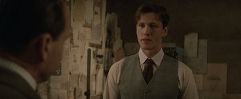 Movie still from “The King's Man” (2021), directed by Matthew Vaughn – A man in a vest and tie standing in front of a wall; Close Up shot, Over the shoulder angle