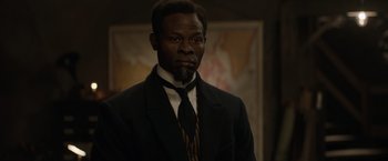 Movie still from “The King's Man” (2021), directed by Matthew Vaughn – A man in a suit and tie standing in front of a painting; Close Up shot, High angle