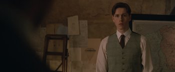 Movie still from “The King's Man” (2021), directed by Matthew Vaughn – A man in a suit and tie standing next to a chair; Close Up shot, Low angle