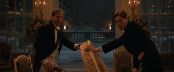 Movie still from “The King's Man” (2021), directed by Matthew Vaughn – A man and a woman in formal attire holding a chair; Medium shot, Low angle