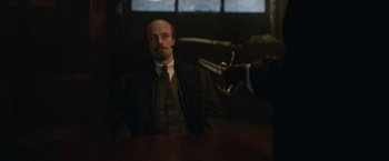 Movie still from “The King's Man” (2021), directed by Matthew Vaughn – A man in a suit and tie sitting at a table; Medium shot, Over the shoulder angle