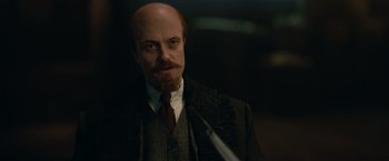 Movie still from “The King's Man” (2021), directed by Matthew Vaughn – A man with a beard and a mustache wearing a suit and tie; Close Up shot, Over the shoulder angle