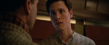 Movie still from “The King's Man” (2021), directed by Matthew Vaughn – A young man looking at the camera while holding his hand up to his face; Close Up shot, Low angle