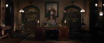 Movie still from “The King's Man” (2021), directed by Matthew Vaughn – A man sitting at a desk in front of a painting; Wide shot, Low angle