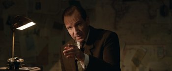 Movie still from “The King's Man” (2021), directed by Matthew Vaughn – A man wearing a suit and tie in a dark room; Close Up shot, Over the shoulder angle