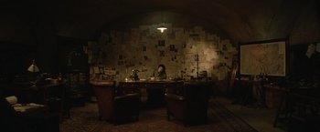 Movie still from “The King's Man” (2021), directed by Matthew Vaughn – A person sitting at a desk in a room with a lot of papers on the wall; Extreme Wide shot, High angle