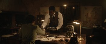 Movie still from “The King's Man” (2021), directed by Matthew Vaughn – A man holding a plate in front of a table; Medium shot, Low angle