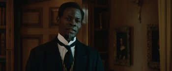 Movie still from “The King's Man” (2021), directed by Matthew Vaughn – A man wearing a suit and tie in a room; Close Up shot, Over the shoulder angle