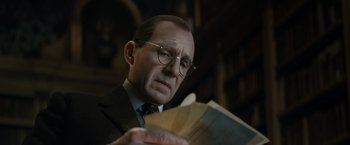 Movie still from “The King's Man” (2021), directed by Matthew Vaughn – An older man in a suit and glasses reading a book; Close Up shot, Low angle