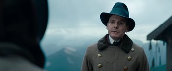 Movie still from “The King's Man” (2021), directed by Matthew Vaughn – A man wearing a green hat and a brown coat; Close Up shot, Over the shoulder angle