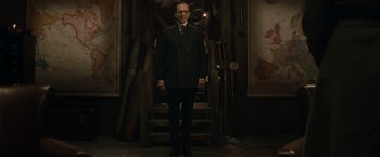 Movie still from “The King's Man” (2021), directed by Matthew Vaughn – A man in a suit standing in front of a staircase; Medium shot, Low angle