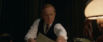 Movie still from “The King's Man” (2021), directed by Matthew Vaughn – A man in a suit and tie holding a newspaper; Close Up shot, Over the shoulder angle