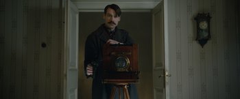 Movie still from “The King's Man” (2021), directed by Matthew Vaughn – A man in a trench coat holding an old fashioned camera; Medium shot, Low angle