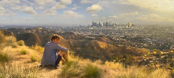 A man sitting on top of a hill looking at a city skyline