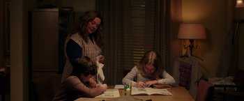 Movie still from “The Kitchen” (2019), directed by Andrea Berloff – A woman and two children sitting at a table doing homework; Medium shot, High angle