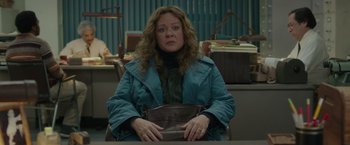 Movie still from “The Kitchen” (2019), directed by Andrea Berloff – A woman sitting at a table holding a brown purse; Medium shot, High angle