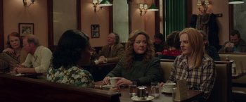 Movie still from “The Kitchen” (2019), directed by Andrea Berloff – A group of people sitting at a table in a restaurant; Medium shot, Over the shoulder angle