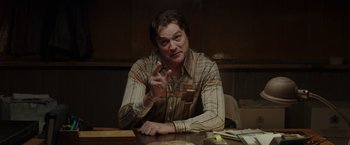 Movie still from “The Kitchen” (2019), directed by Andrea Berloff – A man sitting at a table with a cigarette in his hand; Medium shot, Low angle