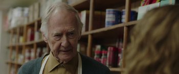 Movie still from “The Kitchen” (2019), directed by Andrea Berloff – An older man standing in front of a shelf of cans; Close Up shot, Over the shoulder angle