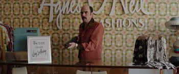 Movie still from “The Kitchen” (2019), directed by Andrea Berloff – A man in a red jacket holding a gun in front of a mirror; Medium shot, Over the shoulder angle