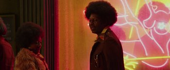 Movie still from “The Kitchen” (2019), directed by Andrea Berloff – A man with a large afro standing in front of a curtain; Medium shot, Over the shoulder angle