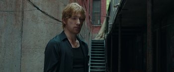 Movie still from “The Kitchen” (2019), directed by Andrea Berloff – A man standing next to stairs in an alleyway; Medium shot, Over the shoulder angle