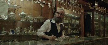 Movie still from “The Kitchen” (2019), directed by Andrea Berloff – A man sitting at a counter in a store; Medium shot, Low angle
