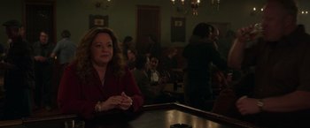 Movie still from “The Kitchen” (2019), directed by Andrea Berloff – A woman sitting at a table in front of a group of people; Medium shot, Over the shoulder angle
