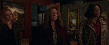 Movie still from “The Kitchen” (2019), directed by Andrea Berloff – A woman standing in front of a painting in a living room; Medium shot, Over the shoulder angle