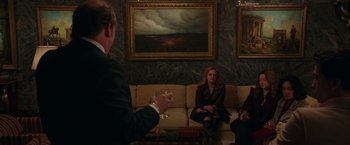 Movie still from “The Kitchen” (2019), directed by Andrea Berloff – A group of people sitting on a couch in front of a painting; Wide shot, Over the shoulder angle