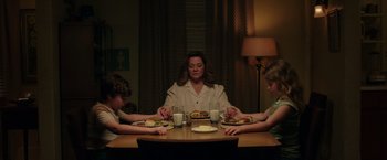 Movie still from “The Kitchen” (2019), directed by Andrea Berloff – A woman sitting at a dinner table with two children; Medium shot, High angle
