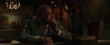 Movie still from “The Kitchen” (2019), directed by Andrea Berloff – An older man talking on a phone while sitting at a table; Medium shot, Low angle