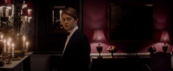 Movie still from “The Last Letter from Your Lover” (2021), directed by Augustine Frizzell – A man in a tuxedo standing next to a lamp; Medium shot, Over the shoulder angle