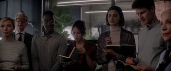 Movie still from “The Last Letter from Your Lover” (2021), directed by Augustine Frizzell – A group of people sitting next to each other holding books; Medium shot, Over the shoulder angle