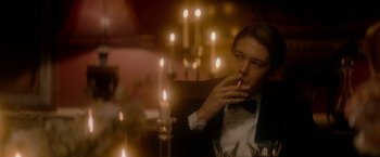 Movie still from “The Last Letter from Your Lover” (2021), directed by Augustine Frizzell – A man smoking a cigarette in front of candles; Medium shot, Over the shoulder angle