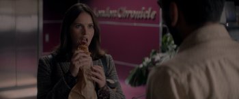 Movie still from “The Last Letter from Your Lover” (2021), directed by Augustine Frizzell – A woman eating a sandwich in front of a sign; Close Up shot, Over the shoulder angle